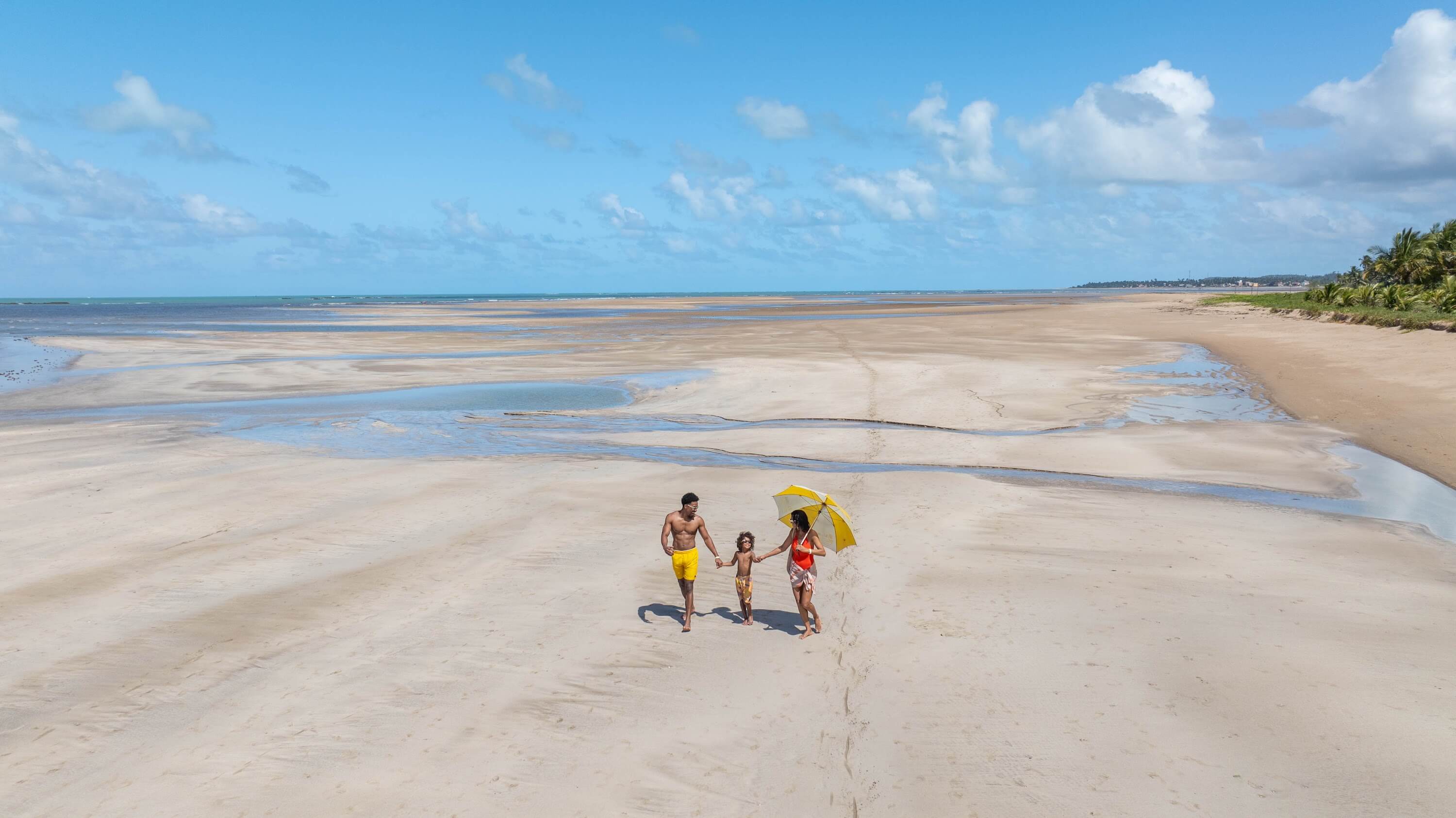 Família passeando na faixa de areia da Praia de Maragogi durante a maré baixa.